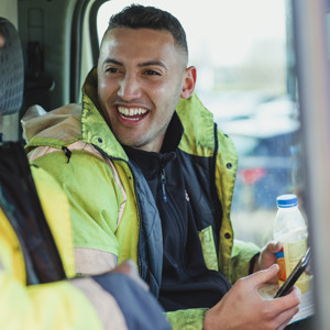 Two Male Labourers Wearing High Vis Jackets Talking And Laughing In Their Work Van Together