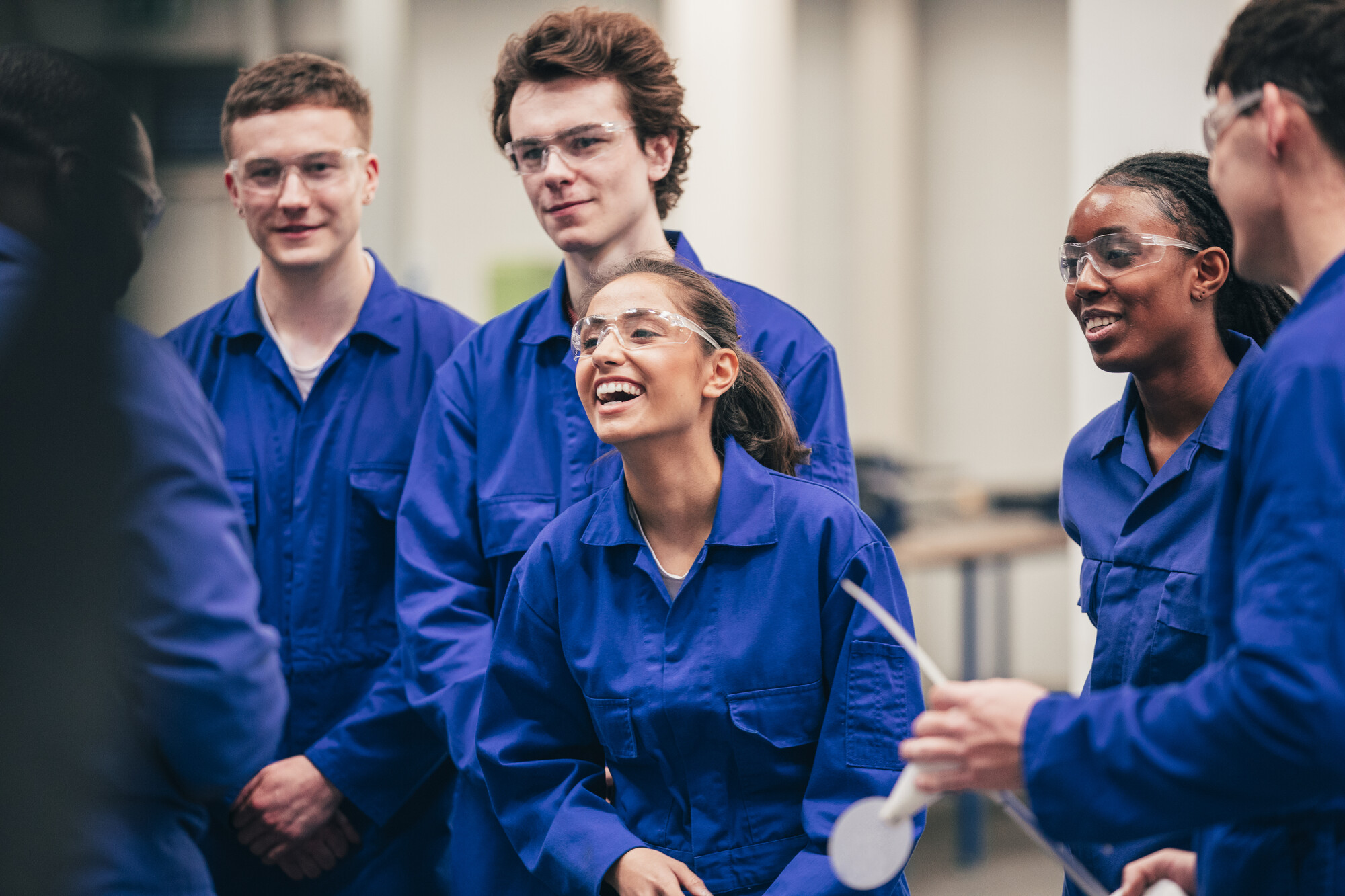 Group of manufacturing students smiling in protective eyewear and lab boilersuits