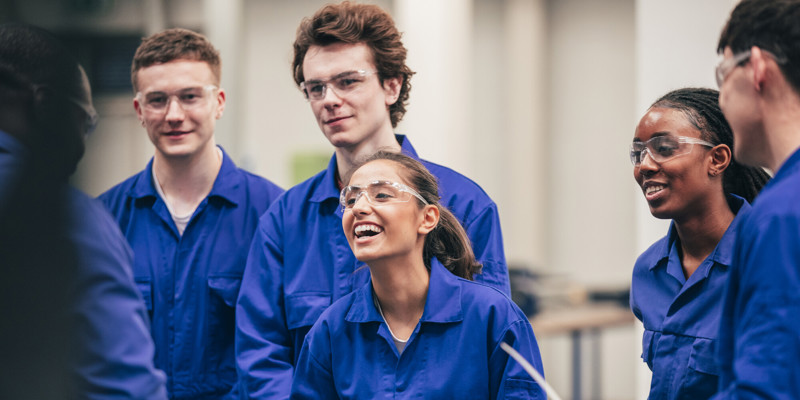 Group of manufacturing students smiling in protective eyewear and lab boilersuits