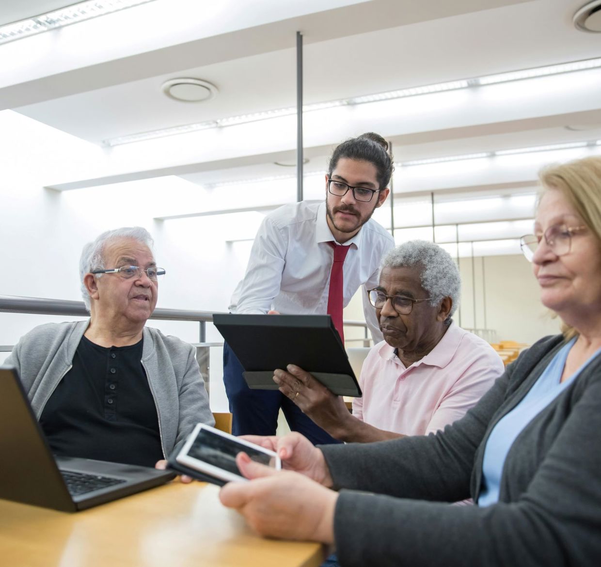 A man showing 3 elderly people how to use a tablet