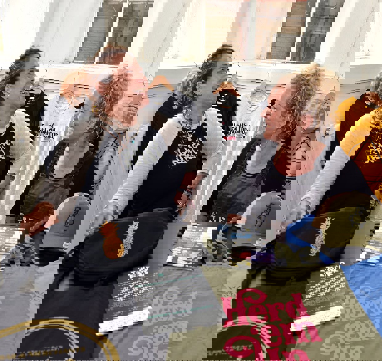 Two ladies laughing with a range of printed merchandise in front of them