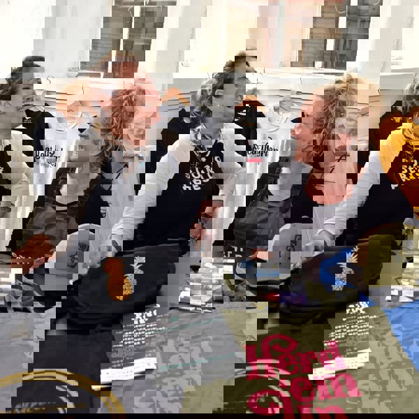 Two ladies laughing with a range of printed merchandise in front of them