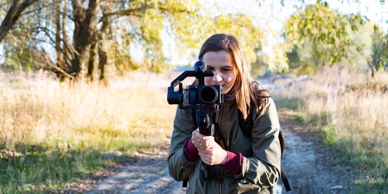 Female Videographer Holding A Gimbal With Camera, Filming Outdoors On A Sunny Afternoon