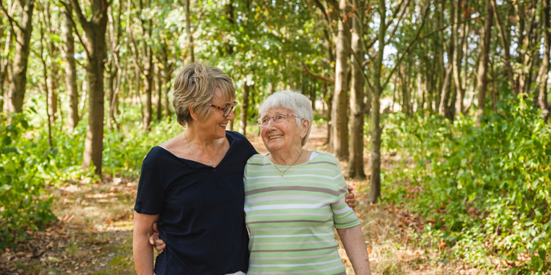 Two Older Women Embracing And Smiling In A Sunny Woodland Stock